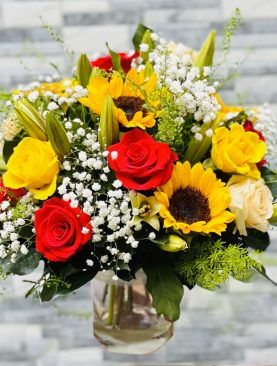 Blooms in shades of red and yellow roses and sunflowers in a glass vase